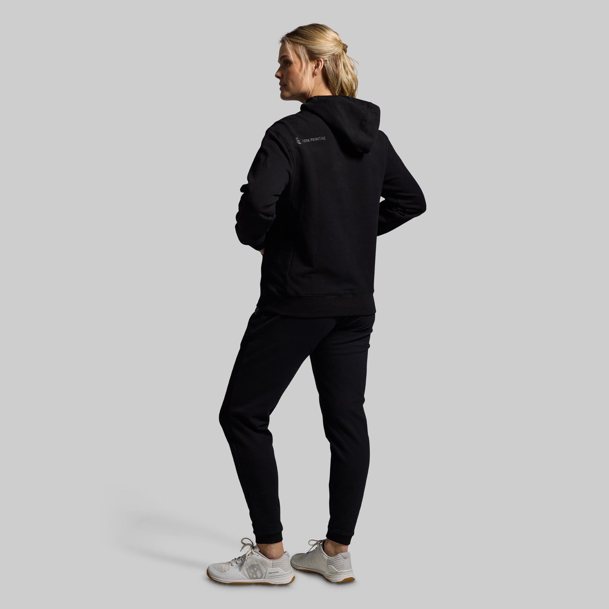 Person wearing a black hoodie and pants with a visible brand logo on a light gray background