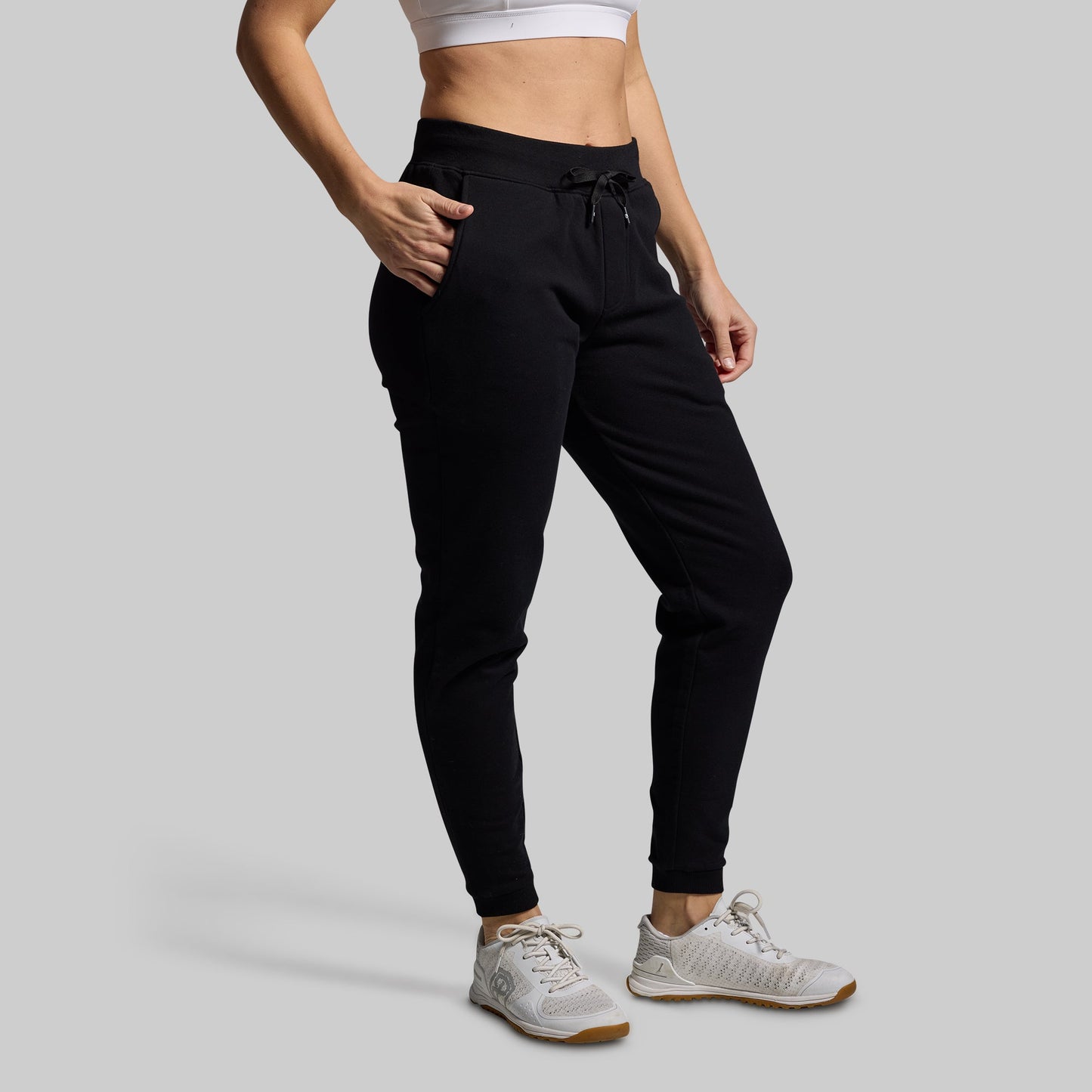 Person wearing black jogger pants and white sneakers on a gray background