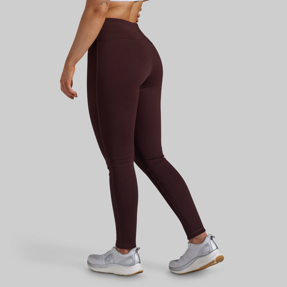 A model wearing high-waisted, form-fitting leggings in a deep burgundy color, shown from a side-rear angle against a solid light gray background.