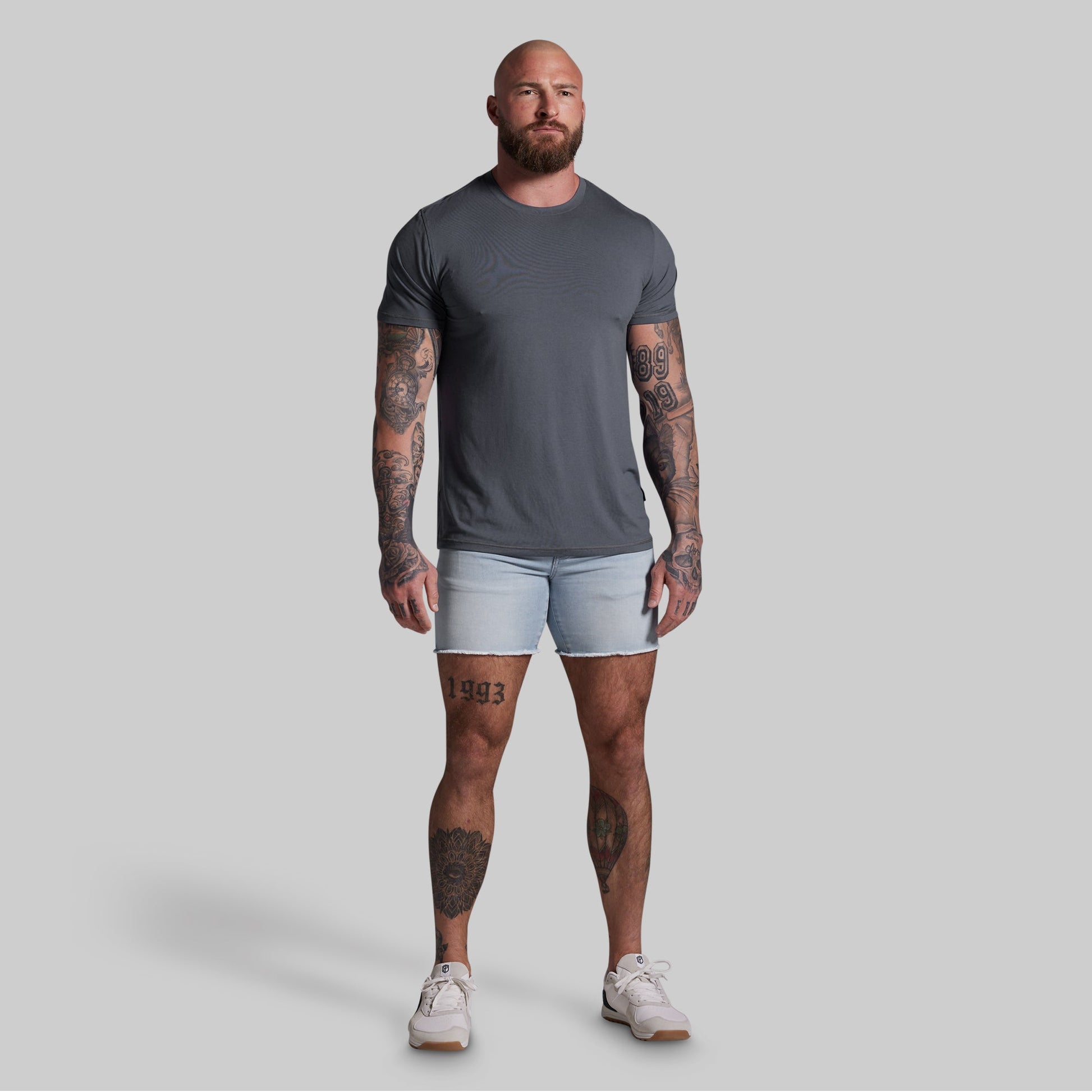 Man wearing a gray t-shirt and light blue shorts on a gray background