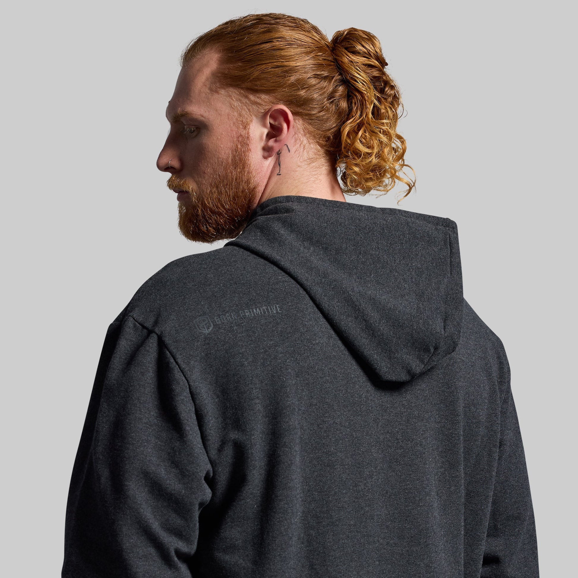 Man wearing a dark gray hoodie with a visible brand logo on the back against a plain background