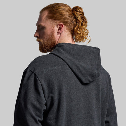 Man wearing a dark gray hoodie with a visible brand logo on the back against a plain background