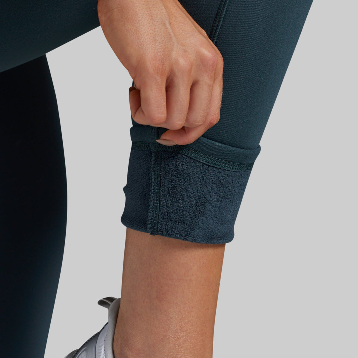 Close-up of a person's hands and lower leg pulling up the cuff of green leggings to reveal a soft, fleece-lined interior.
