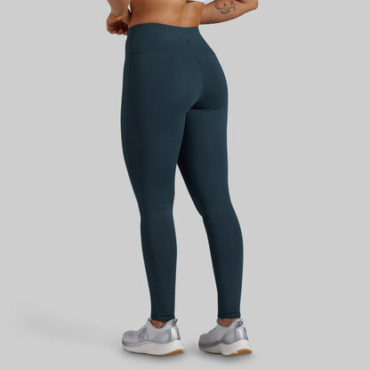 Back view of a model wearing high-waisted dark teal blue-gray leggings against a light gray studio background.