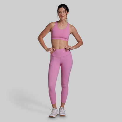 Woman wearing a pink sports bra and leggings set on a gray background