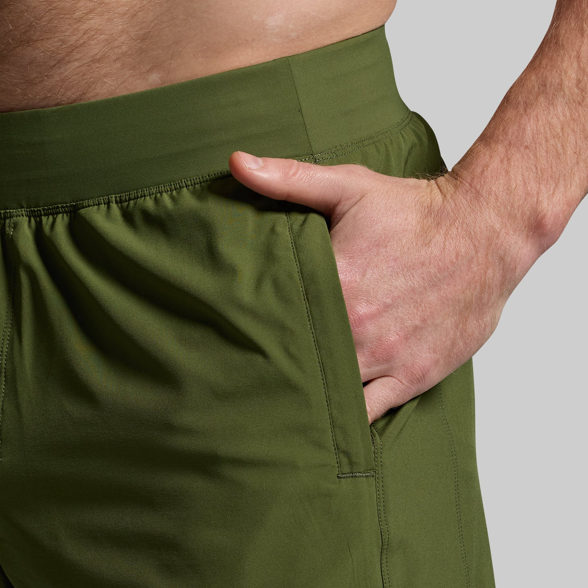 A close-up image of a person's hand in the pocket of a military green athletic training short.