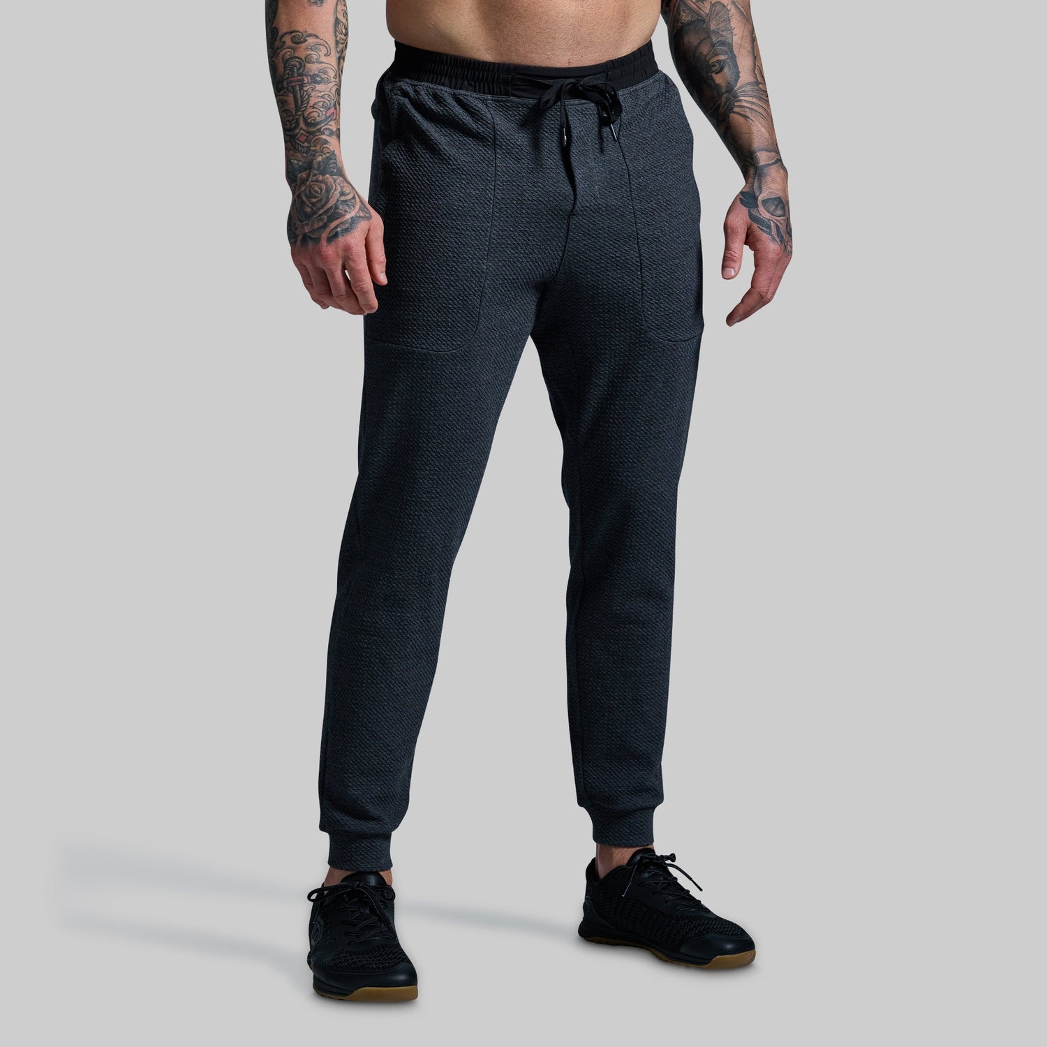 Person wearing dark gray jogger pants on a light gray background