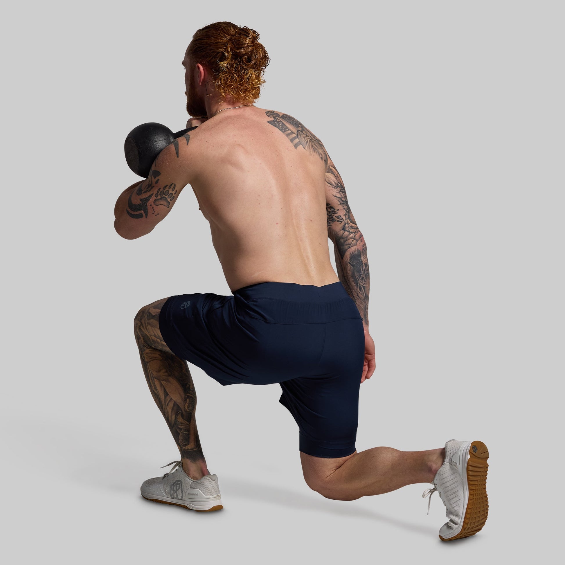 Man performing a squat exercise with a kettlebell wearing navy blue shorts on a gray background