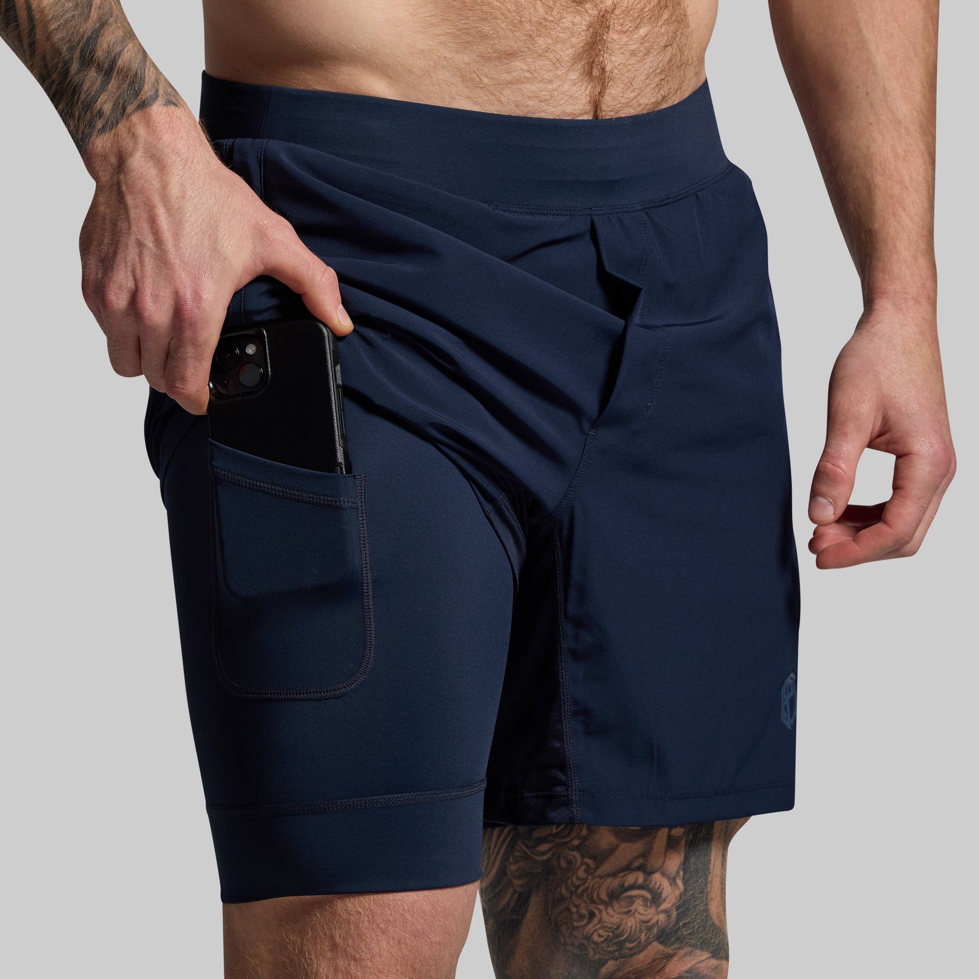 Person pulling phone out of pocket in compression lining of navy blue athletic shorts on a gray background