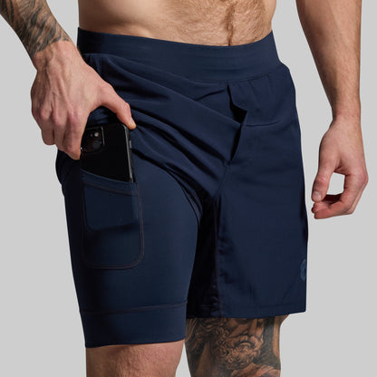 Person pulling phone out of pocket in compression lining of navy blue athletic shorts on a gray background