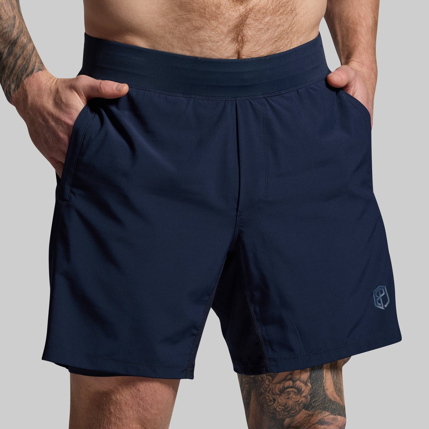Navy blue shorts worn by a person standing with hands in pockets on a gray background