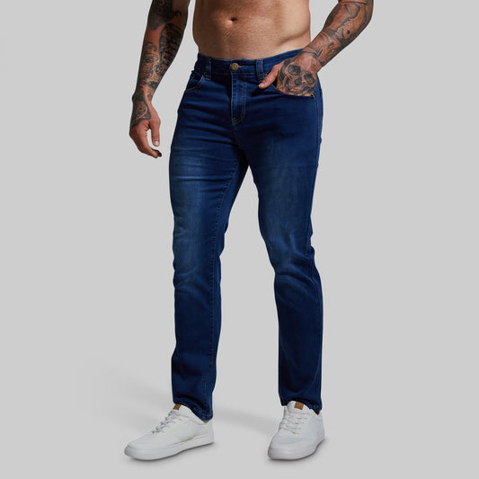 A male model wearing dark wash stretchy athletic fit jeans and white sneakers.