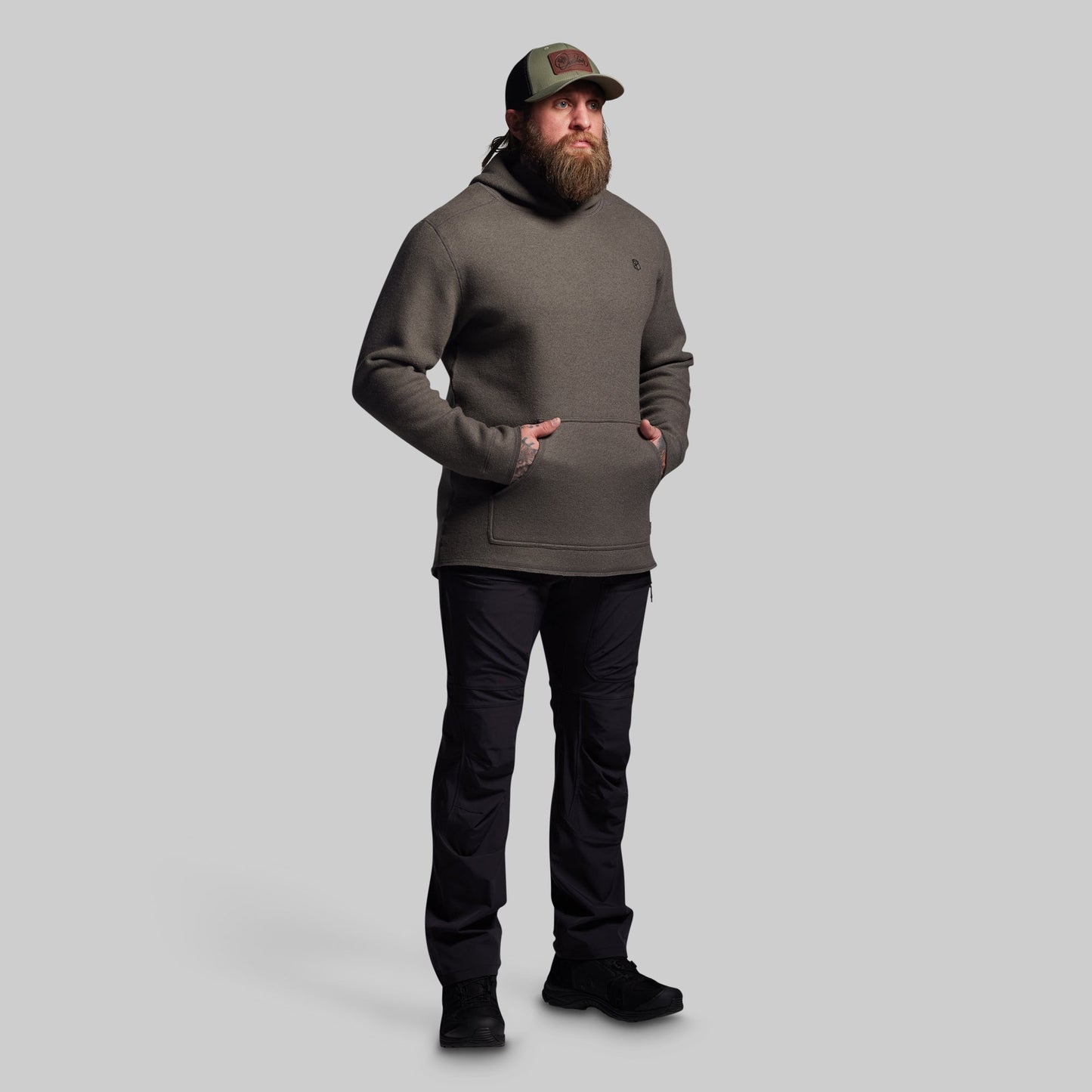 Man wearing a dark gray hoodie and black pants on a light gray background
