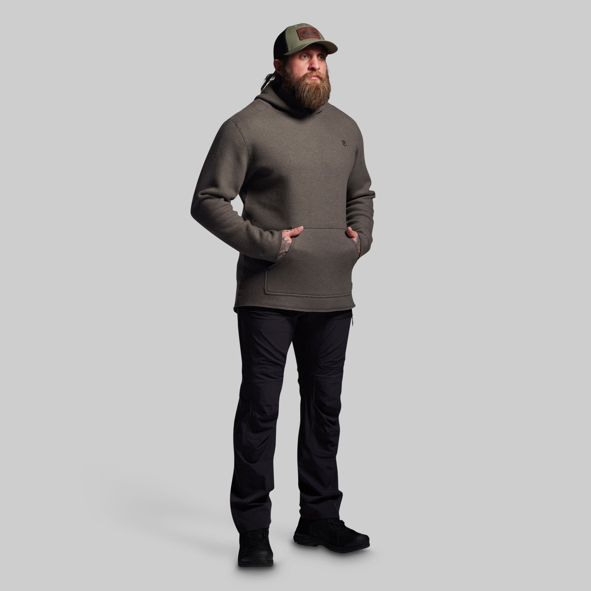 Man wearing a dark gray hoodie and black pants on a light gray background
