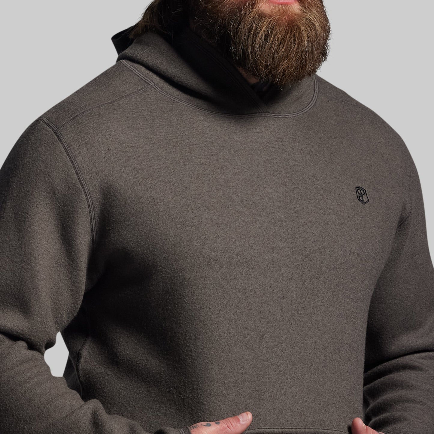 Person wearing a dark gray hoodie with a small logo on a light gray background