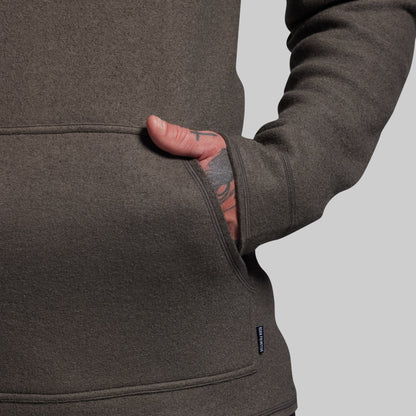 Close-up of a person wearing a gray hoodie with a visible brand logo on a light gray background