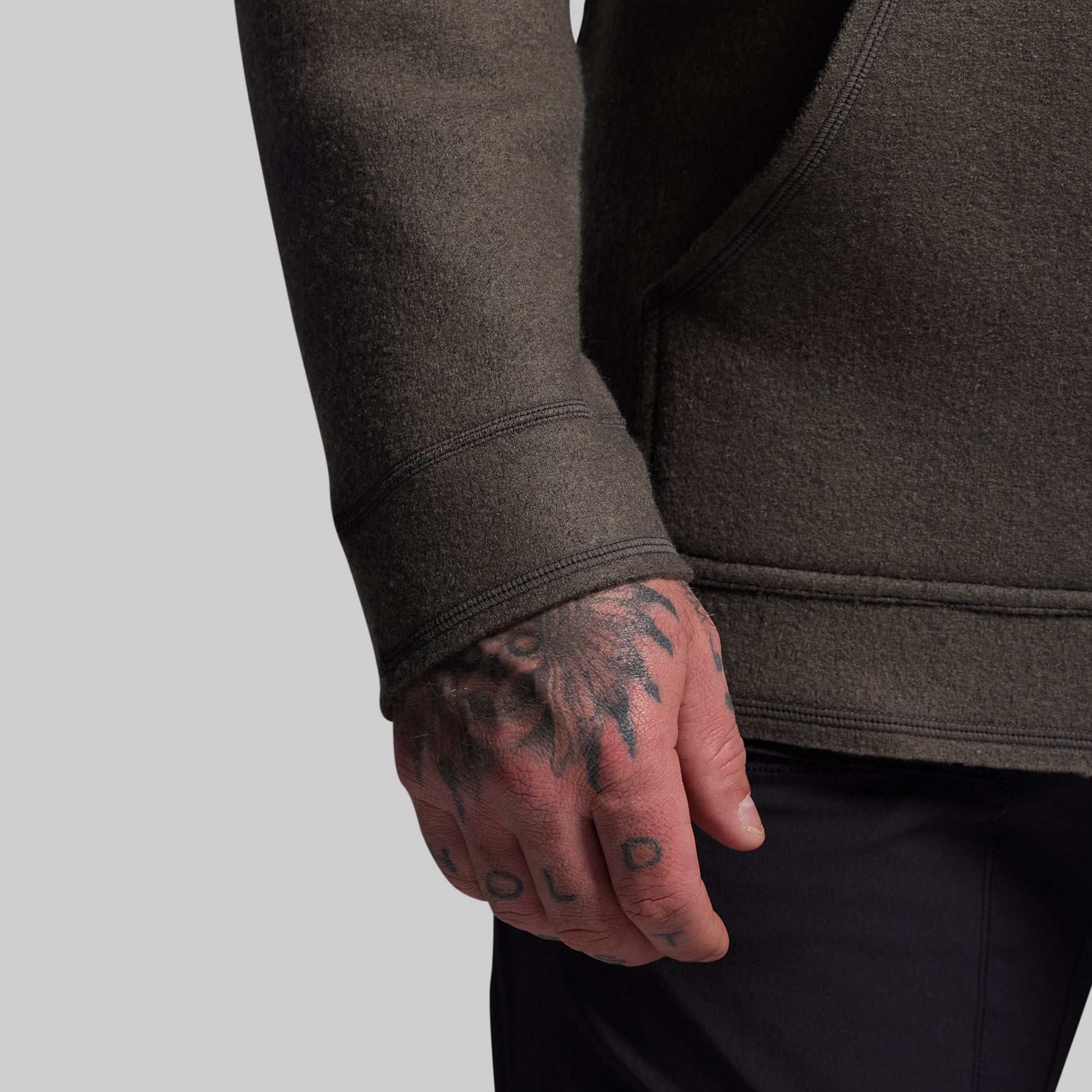 Person wearing a dark gray hoodie with a tattooed hand on a light gray background