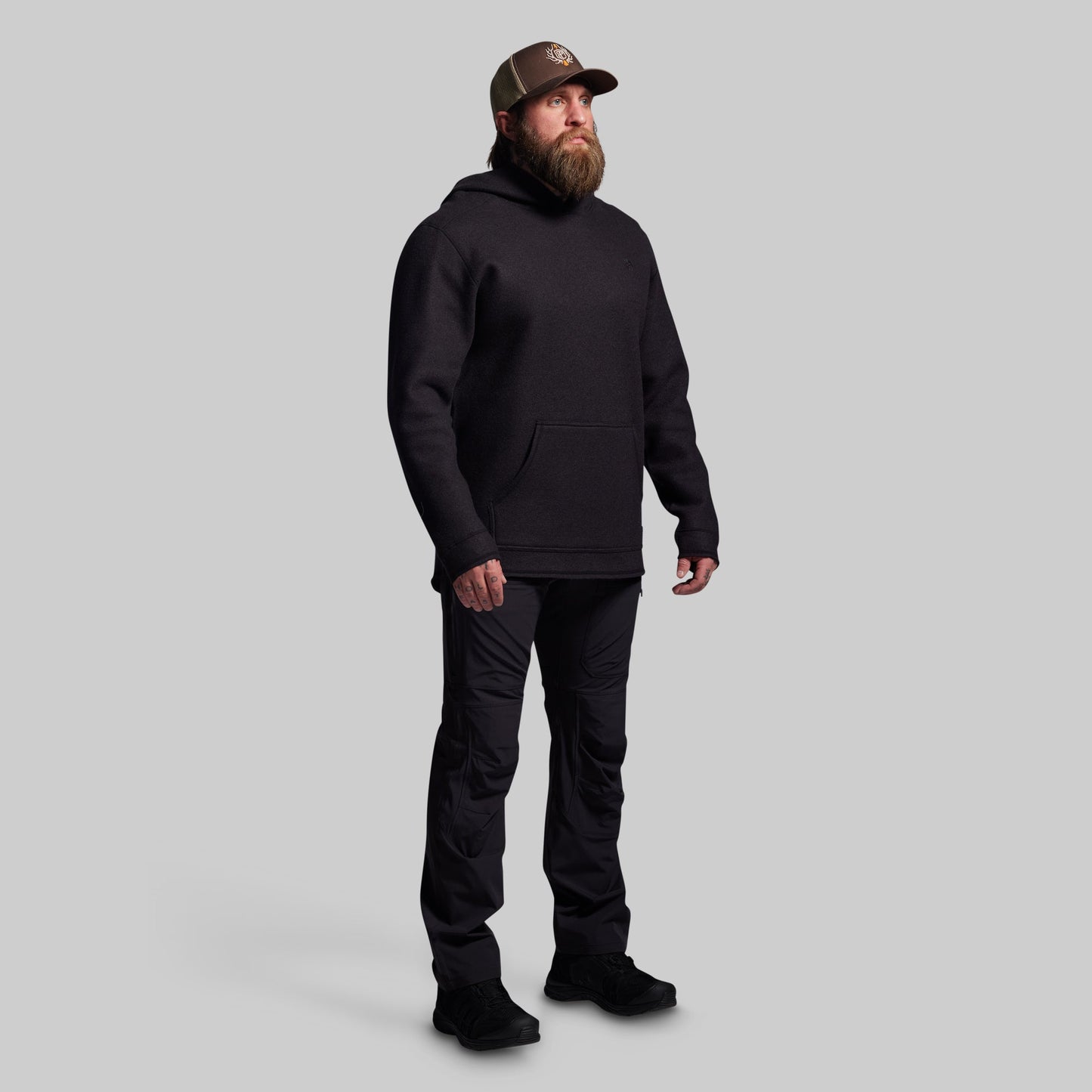 Man wearing a black hoodie, pants, and boots on a gray background