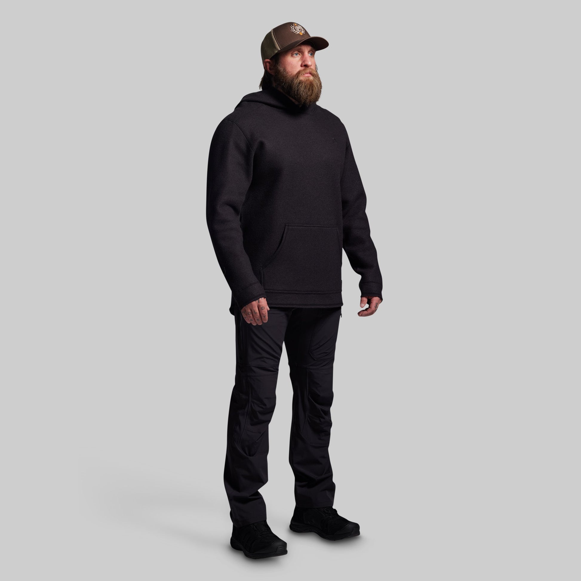 Man wearing a black hoodie, pants, and boots on a gray background
