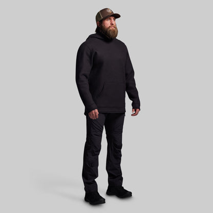 Man wearing a black hoodie, pants, and boots on a gray background