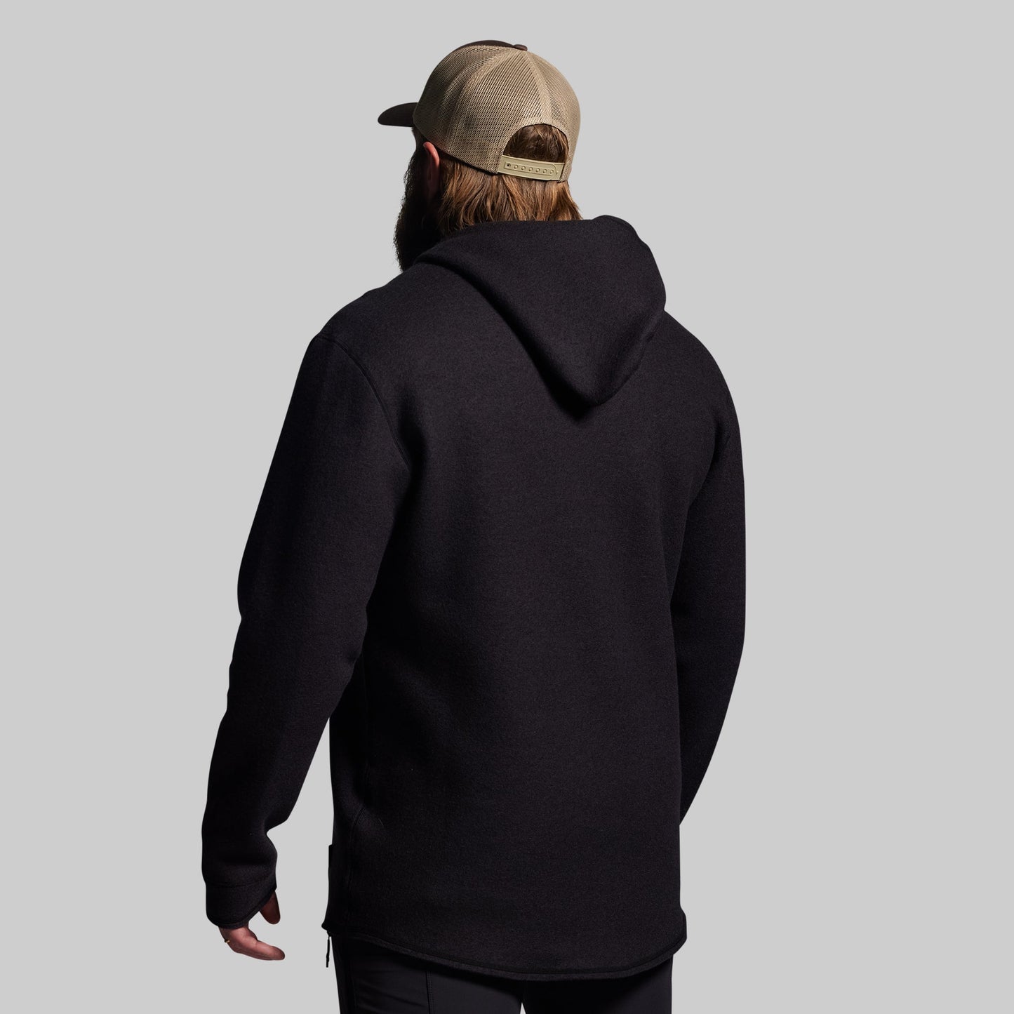 Person wearing a black hoodie and a cap from behind on a gray background