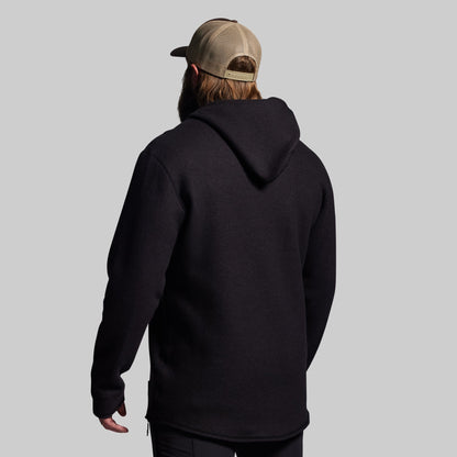Person wearing a black hoodie and a cap from behind on a gray background