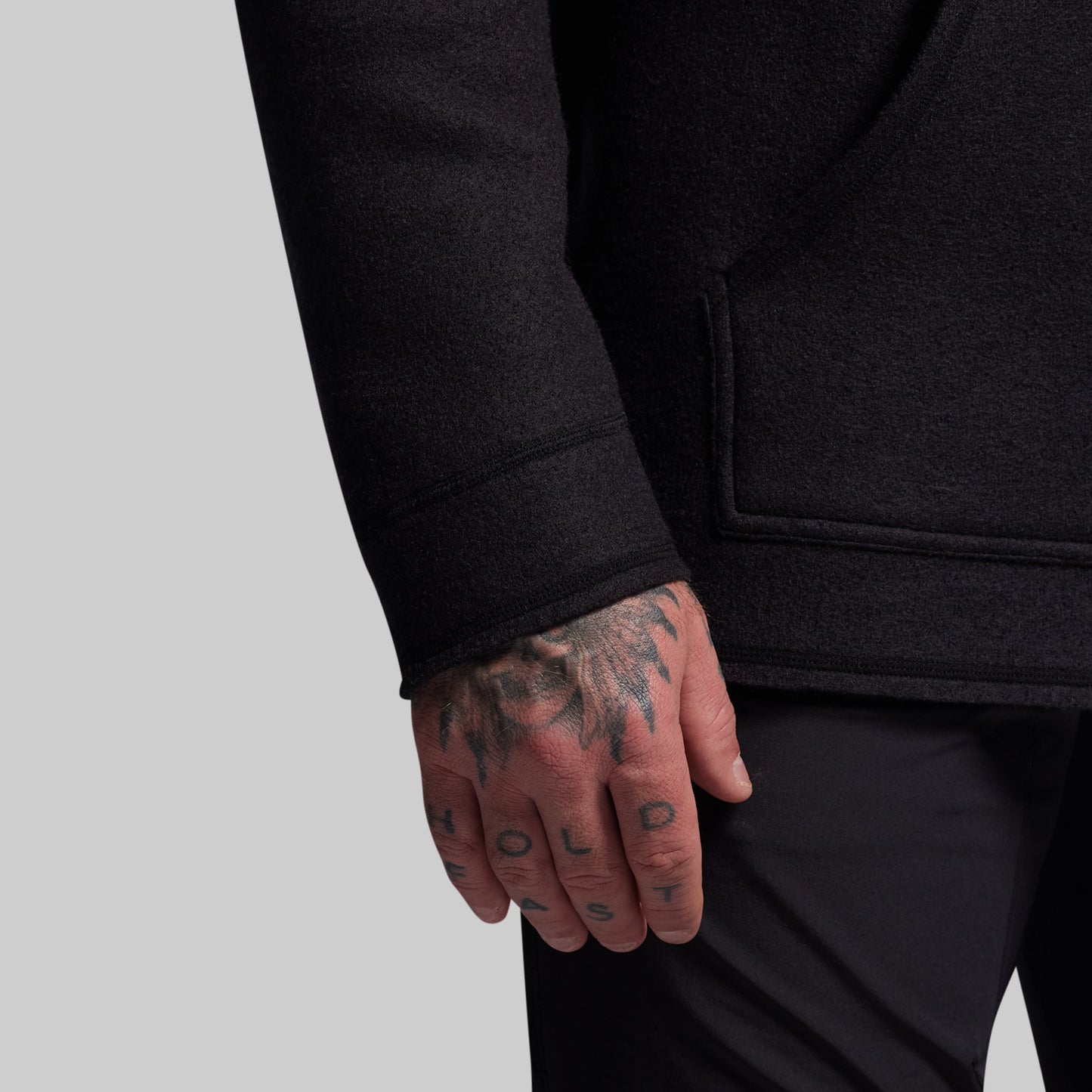 Person wearing a black hoodie with tattooed hand on a light gray background
