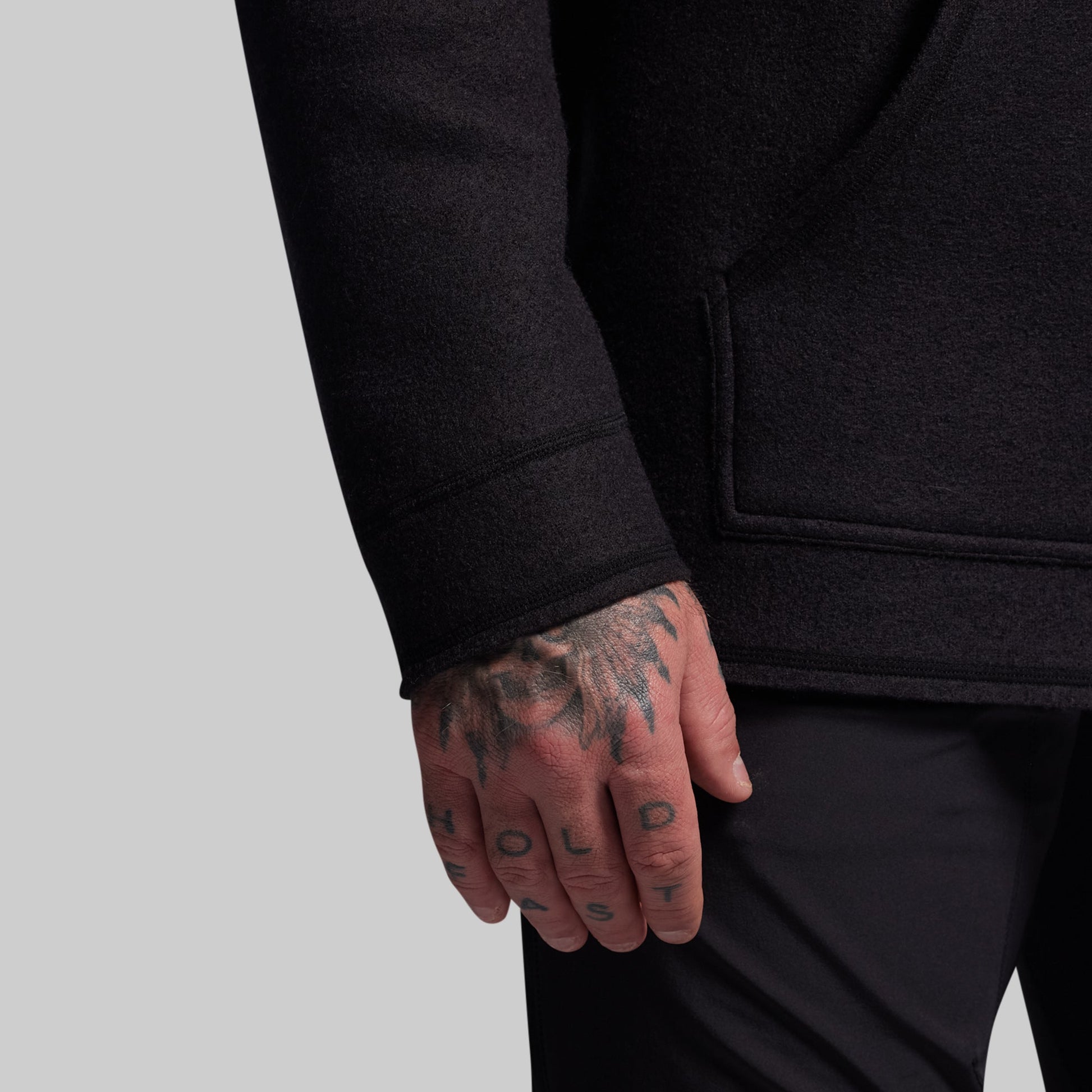 Person wearing a black hoodie with tattooed hand on a light gray background