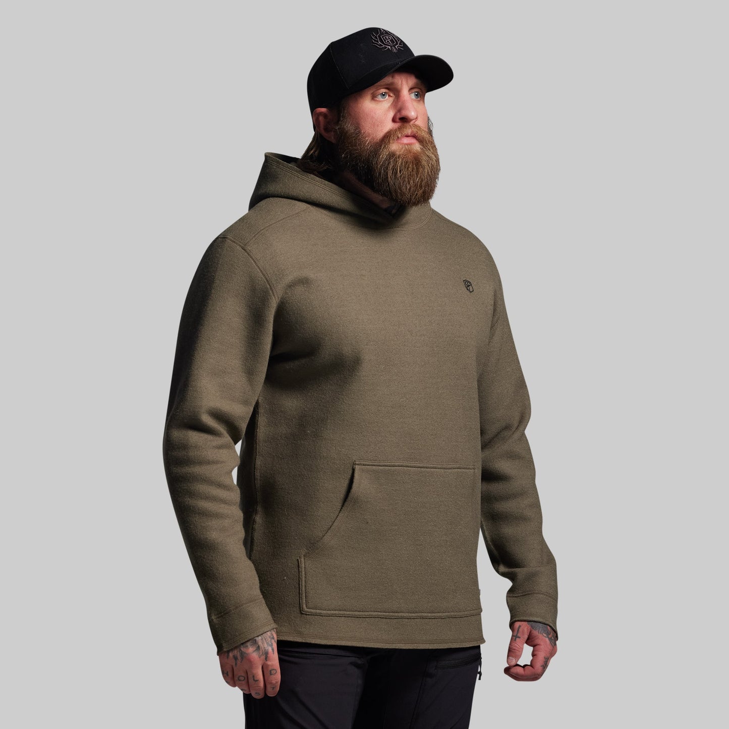Man wearing a green hoodie and black cap on a gray background