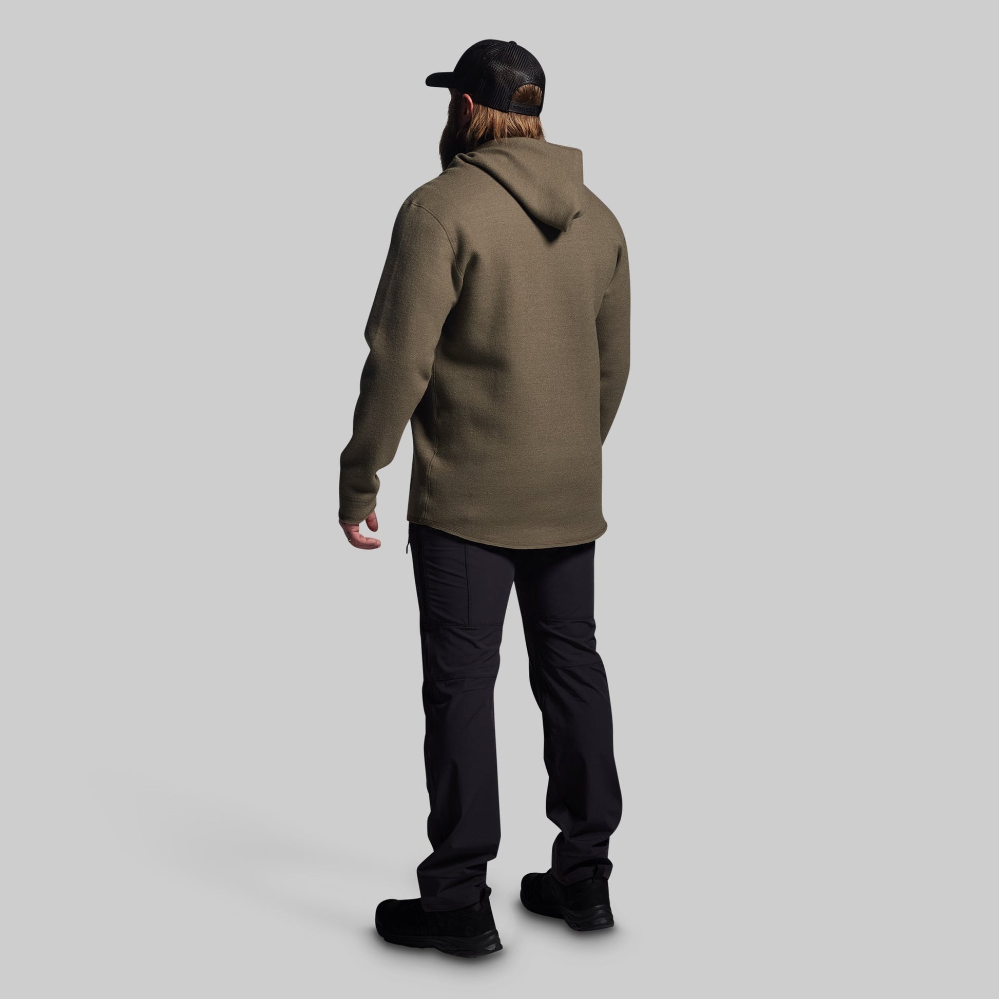 Person wearing a green hoodie and black pants on a light gray background
