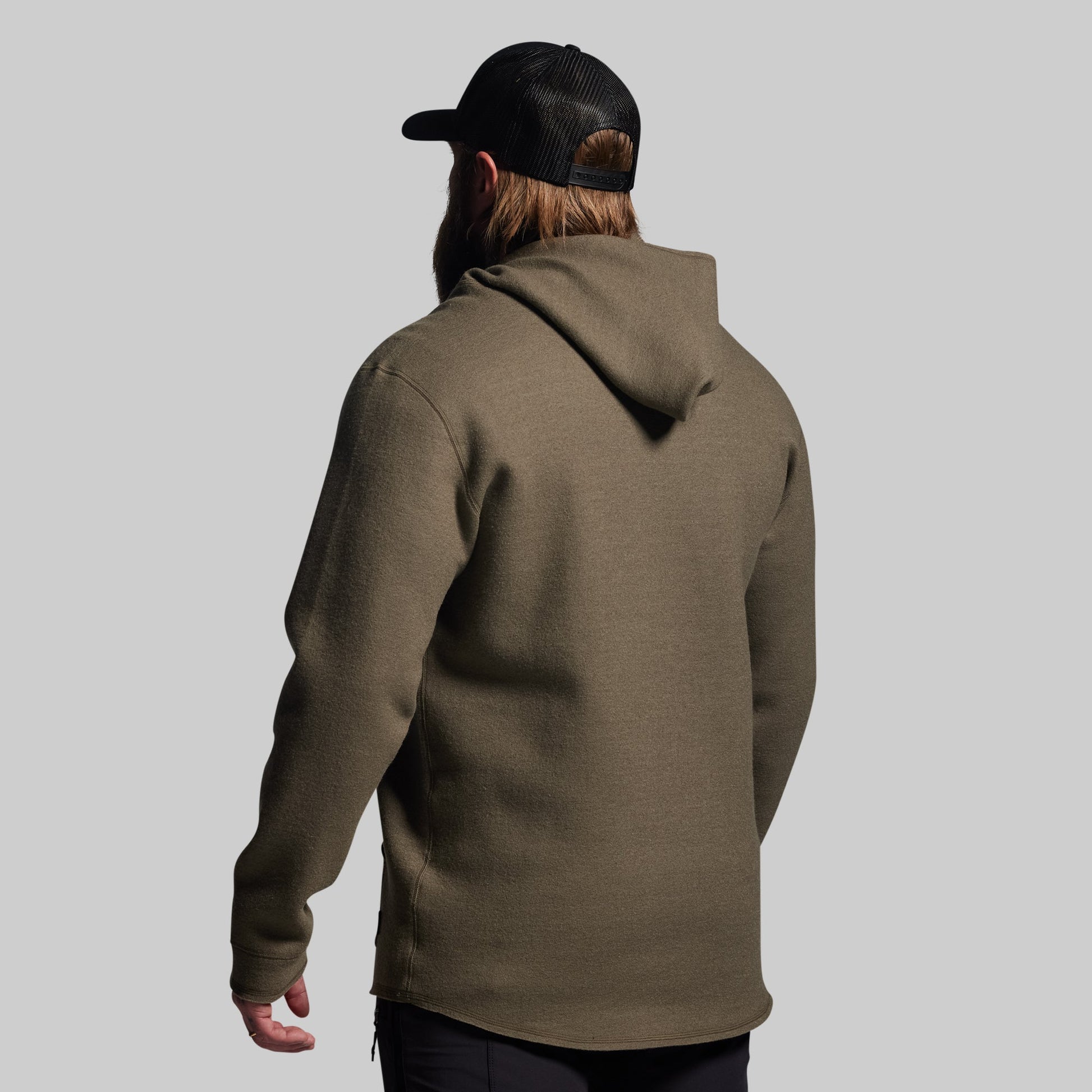 Person wearing a green hoodie and black cap from behind on a gray background