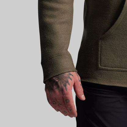 Person wearing a dark green hoodie with a tattooed hand on a gray background