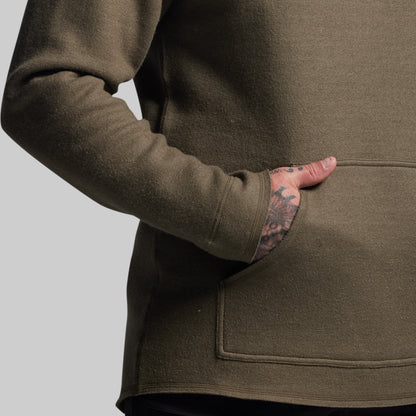 Person wearing a green hoodie with a tattooed arm on a gray background