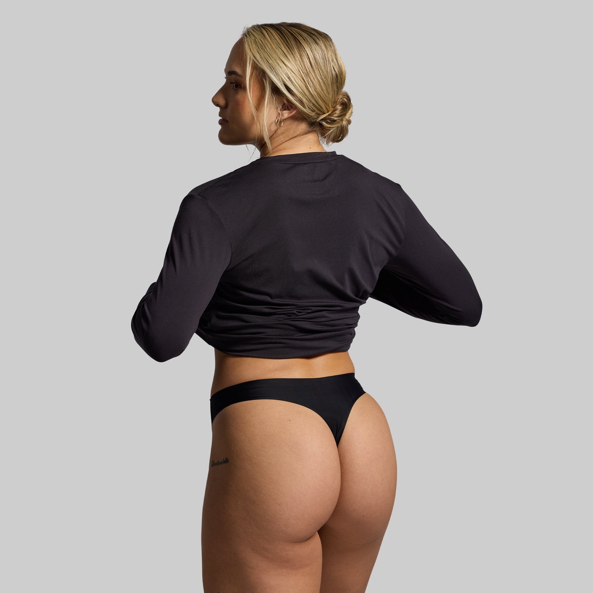 Woman wearing a black long-sleeve top and black thong on a gray background