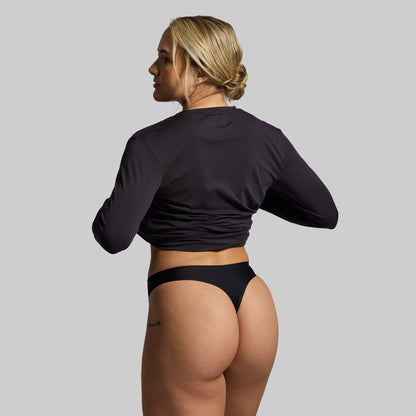 Woman wearing a black long-sleeve top and black thong on a gray background