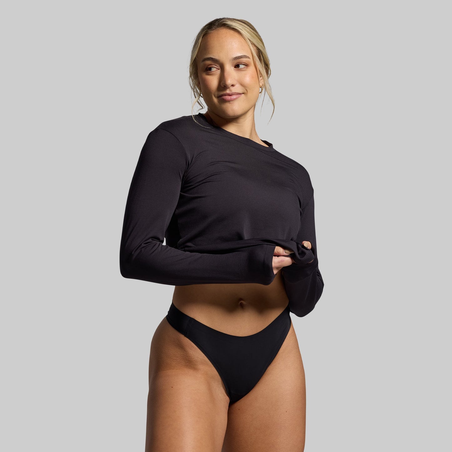Woman wearing a black long-sleeve top and black underwear on a gray background