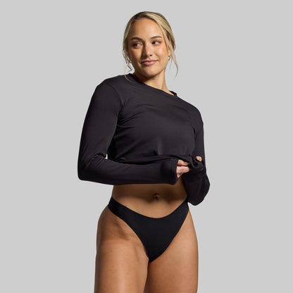 Woman wearing a black long-sleeve top and black underwear on a gray background