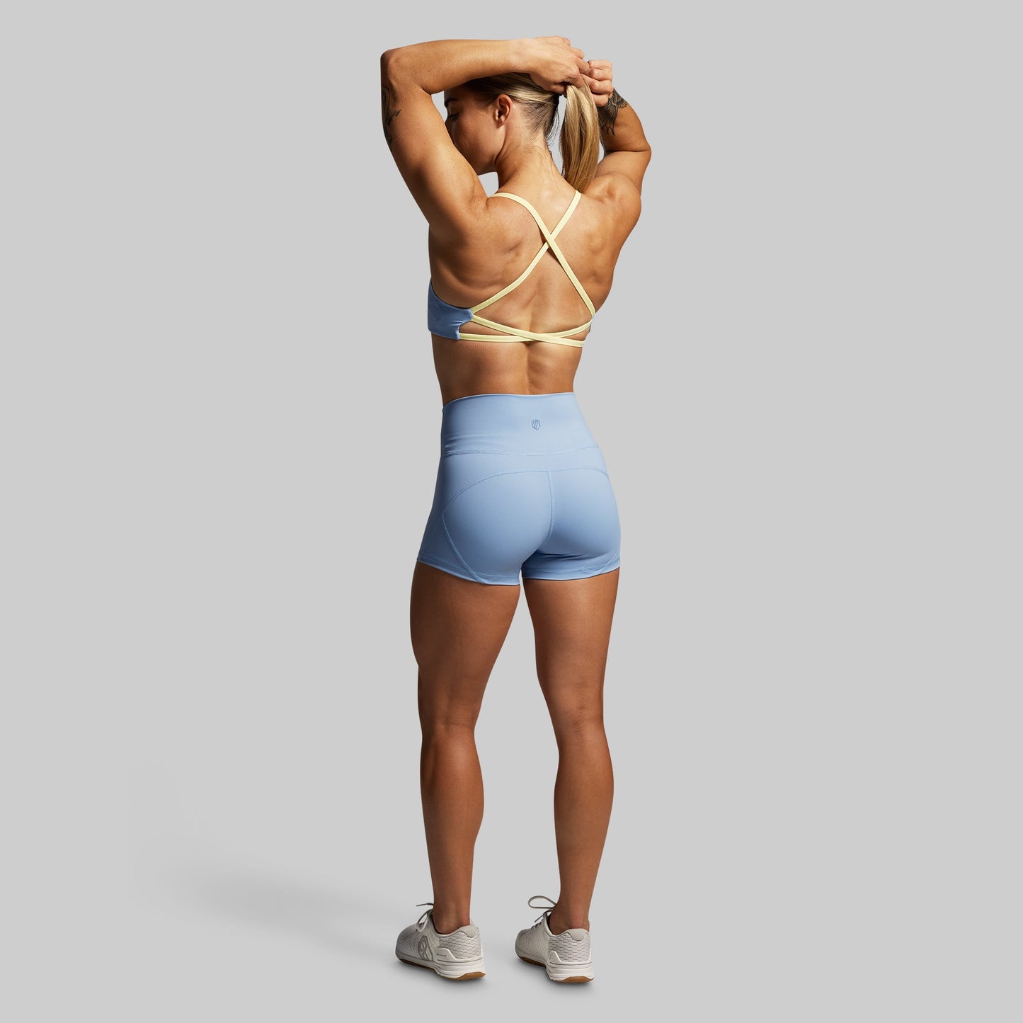 Woman in blue athletic shorts and sports bra posing against a gray background