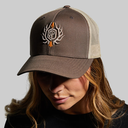 Person wearing a brown and beige cap with a logo on a gray background