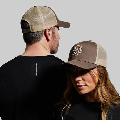 A man and a woman wearing brown trucker hats with tan mesh. The hats feature an outdoor brand logo on the front.