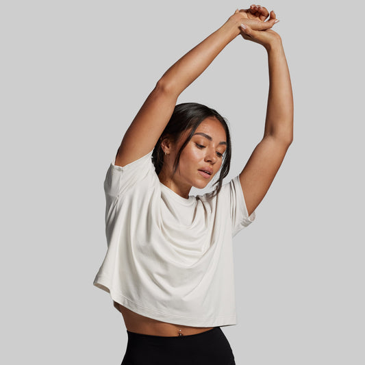 Woman in a white shirt and black pants stretching against a plain background