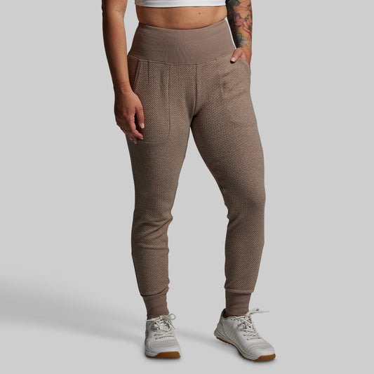 Person wearing brown textured jogger pants on a gray background