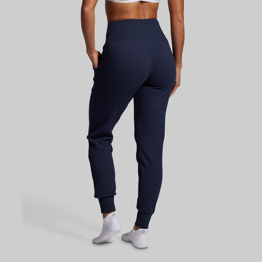 Person wearing navy blue jogger pants on a gray background