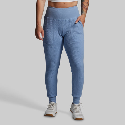 Person wearing blue textured jogger pants on a gray background