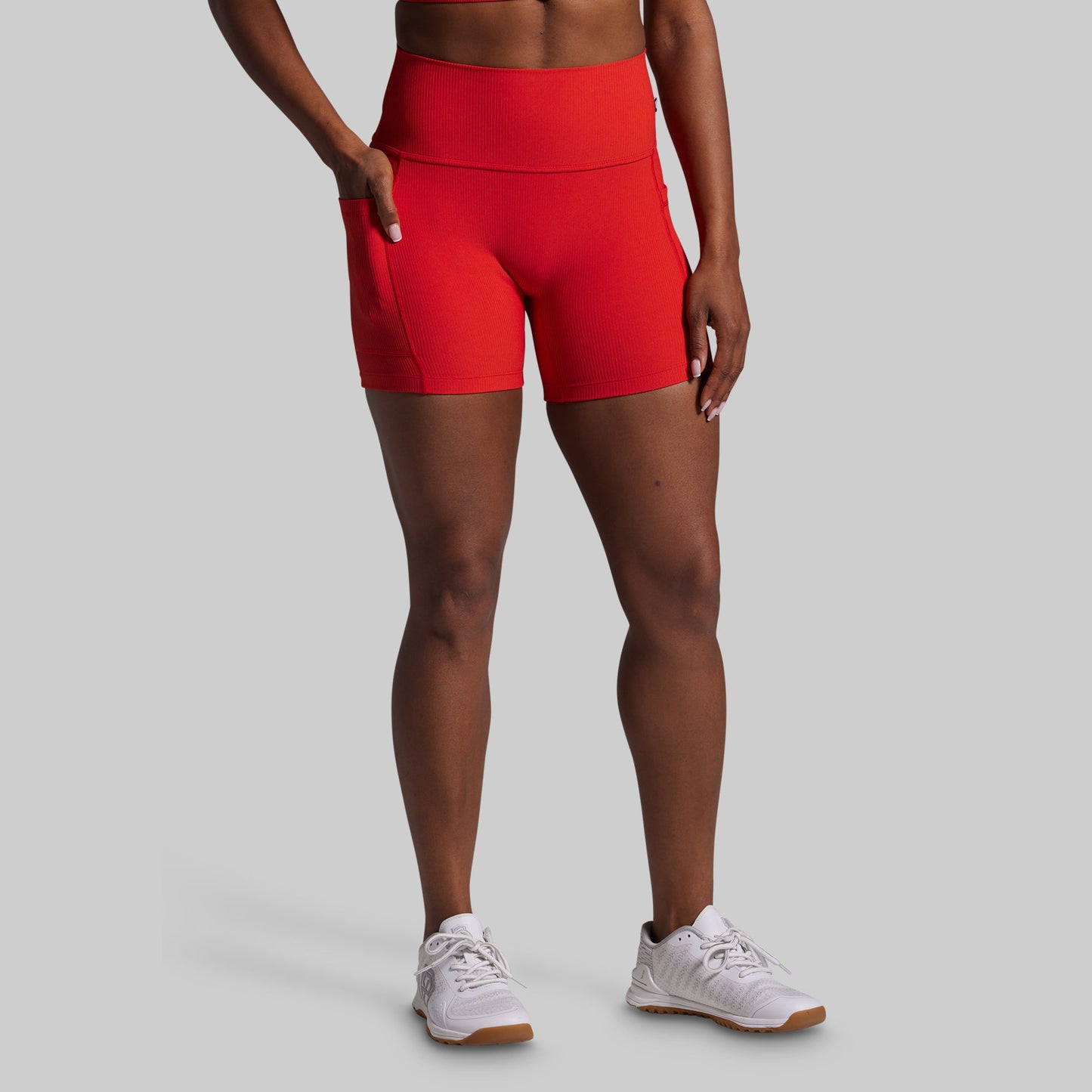 Person wearing red athletic shorts and white sneakers on a gray background