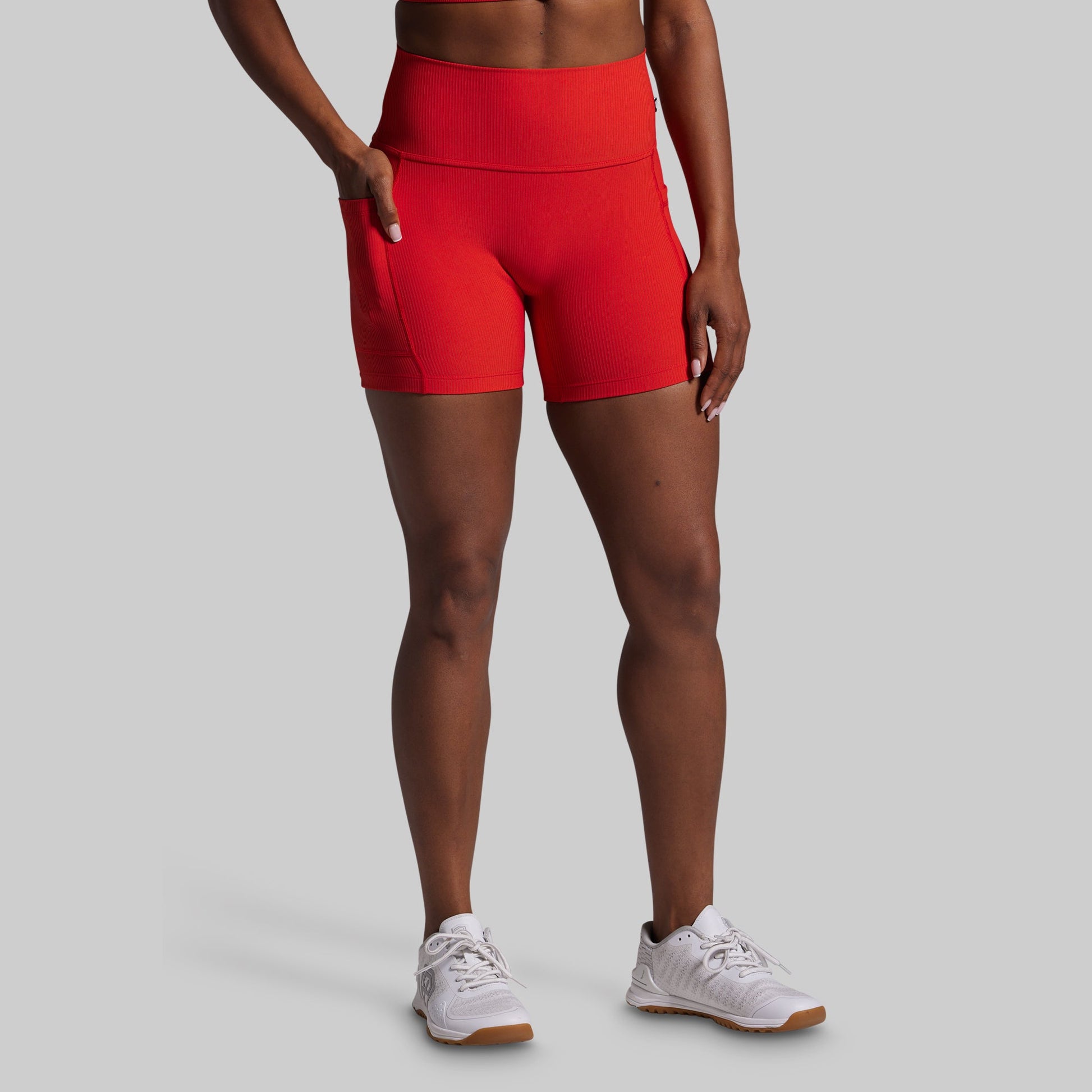 Person wearing red athletic shorts and white sneakers on a gray background
