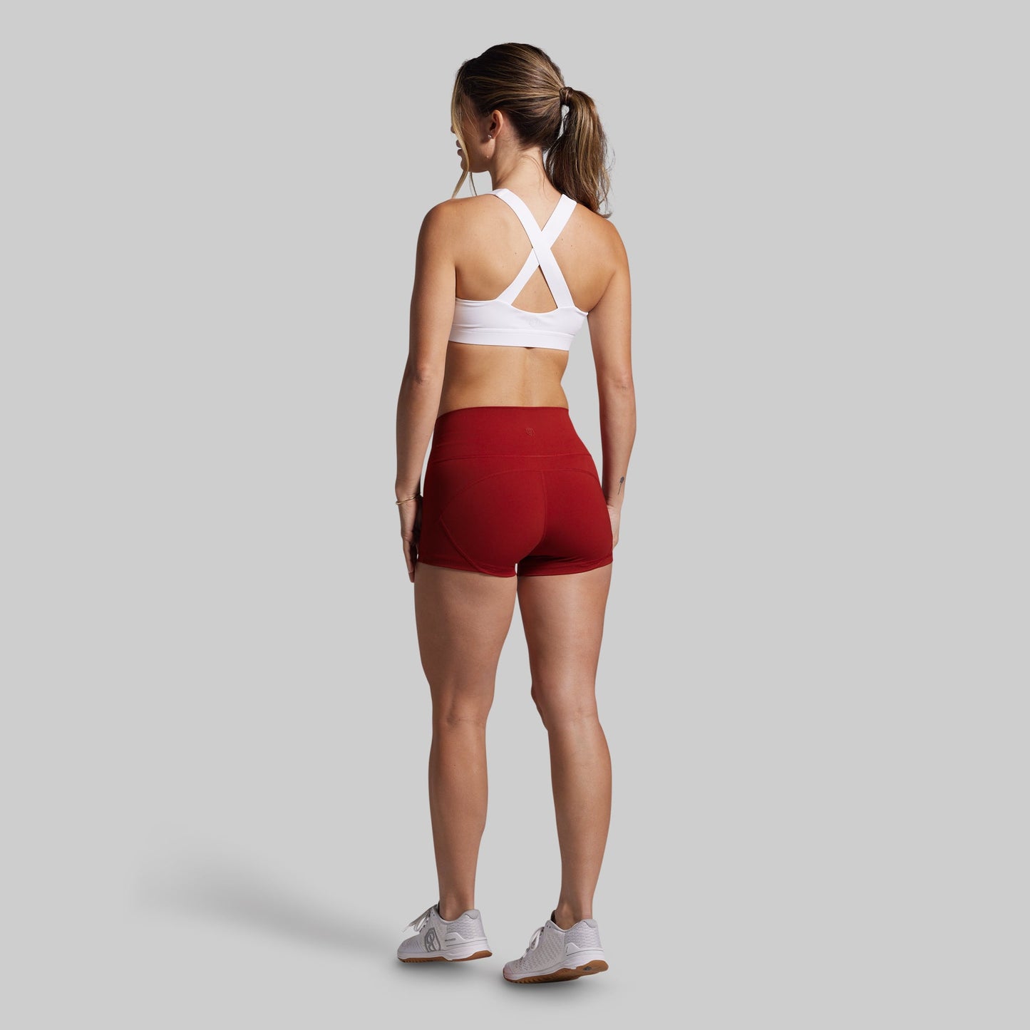 Woman wearing a white sports bra and red shorts on a gray background