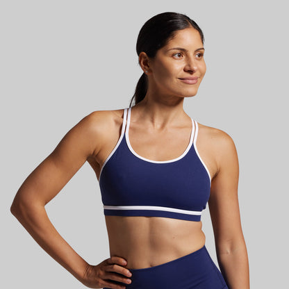 Woman wearing a blue sports bra with white straps on a gray background