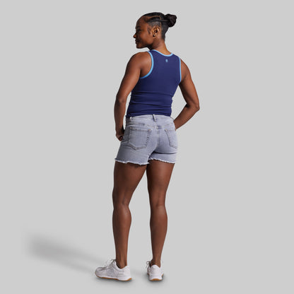 Woman wearing a blue tank top and denim shorts on a gray background
