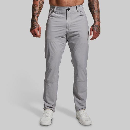 A male model wearing a pair of gray Traverse Pants with a button-and-fly closure, front pockets, and a regular fit.